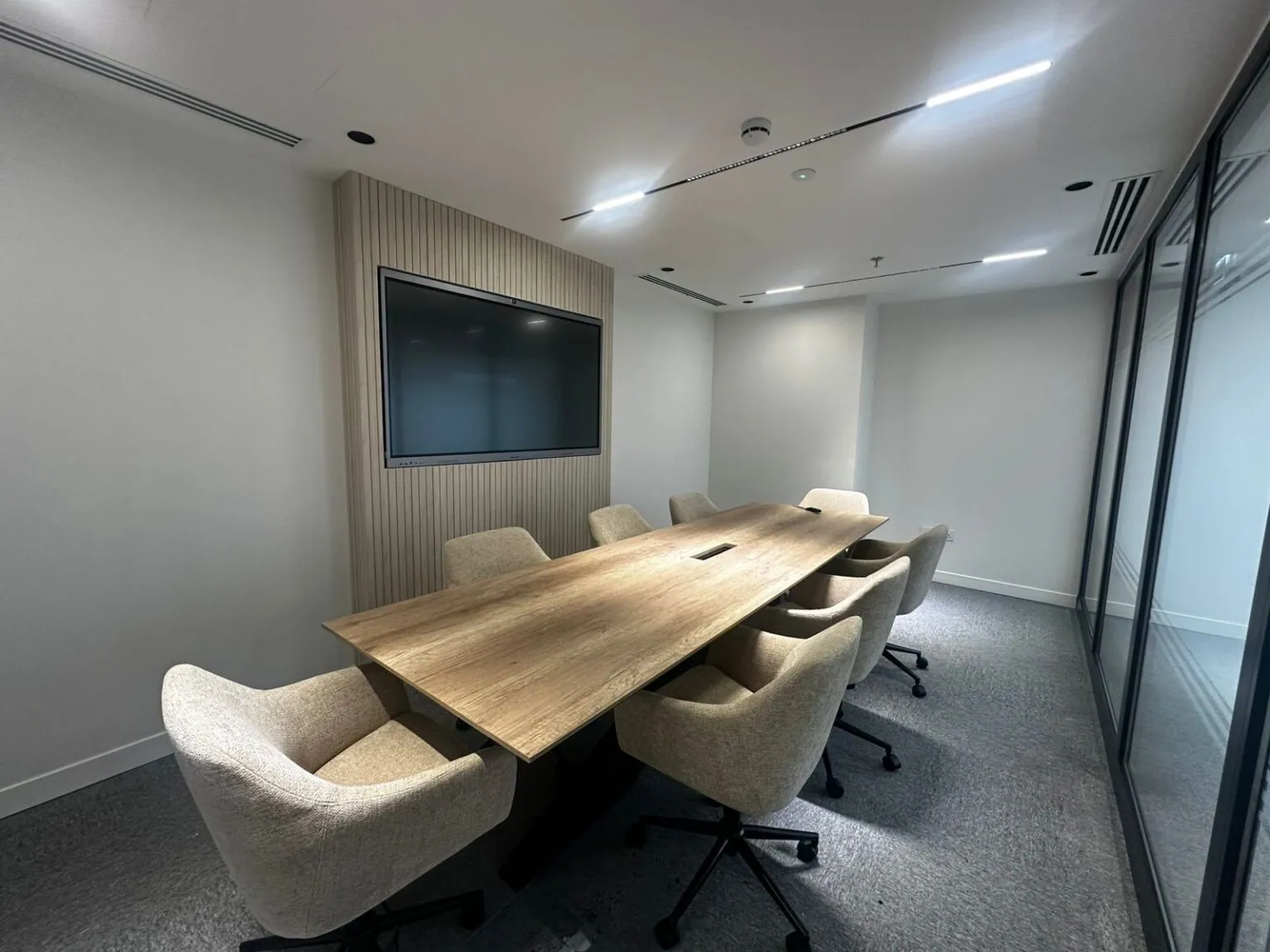 A Privé Lounge meeting room with a wall-mounted presentation screen and seating for eight